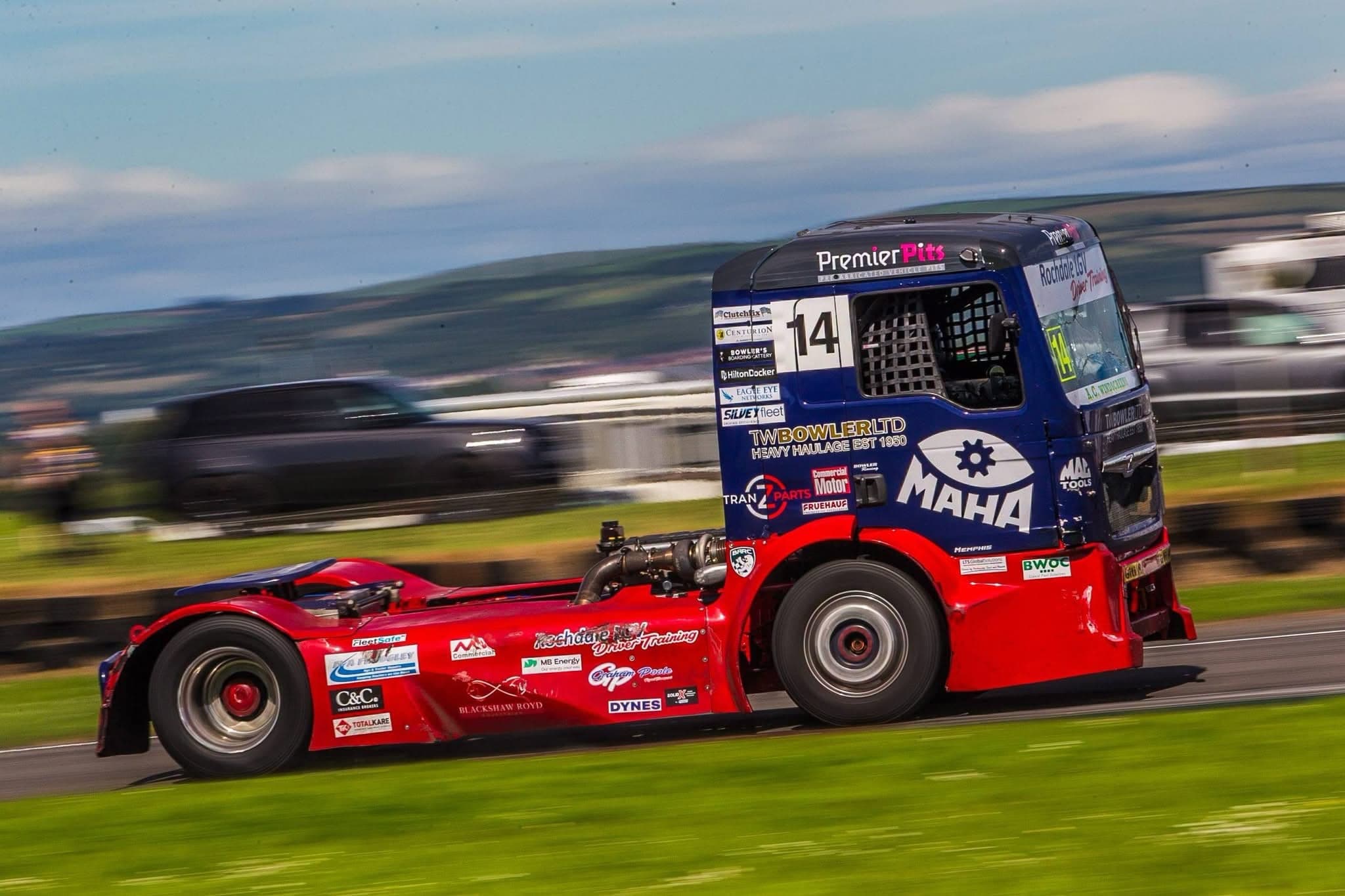 Diana, number 14, panned side-on at speed, her door number and partner livery sharp against streaked green hills