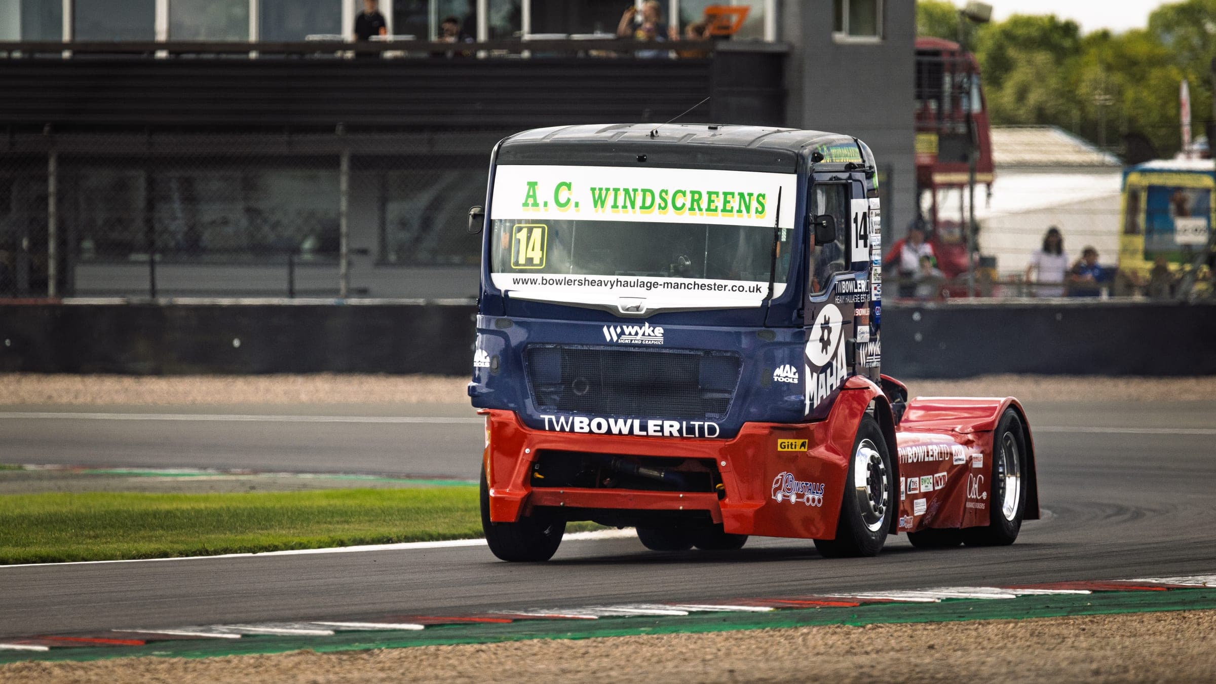 Diana, number 14, cornering towards the camera in her A.C. Windscreens livery, kerb and gravel in the foreground