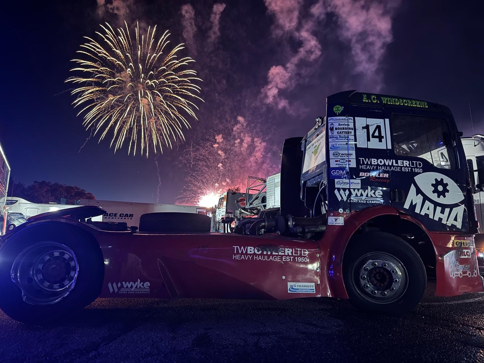 Diana, number 14, parked side-on in the paddock at night as a gold firework bursts in the sky above