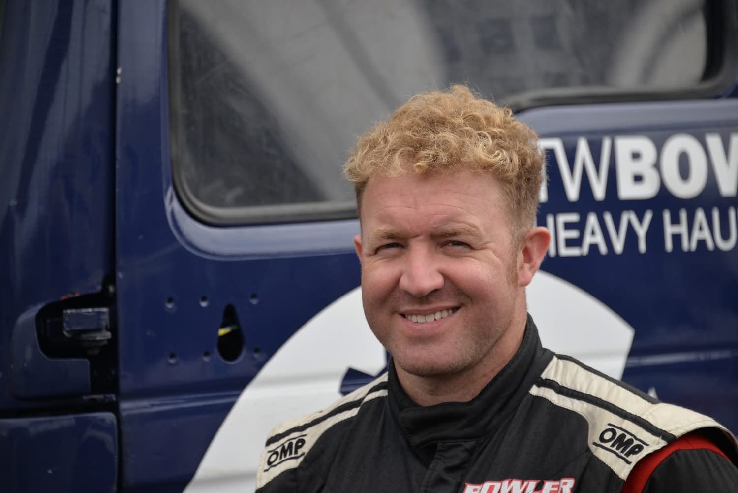 Close portrait of John Bowler smiling in his race suit beside the truck